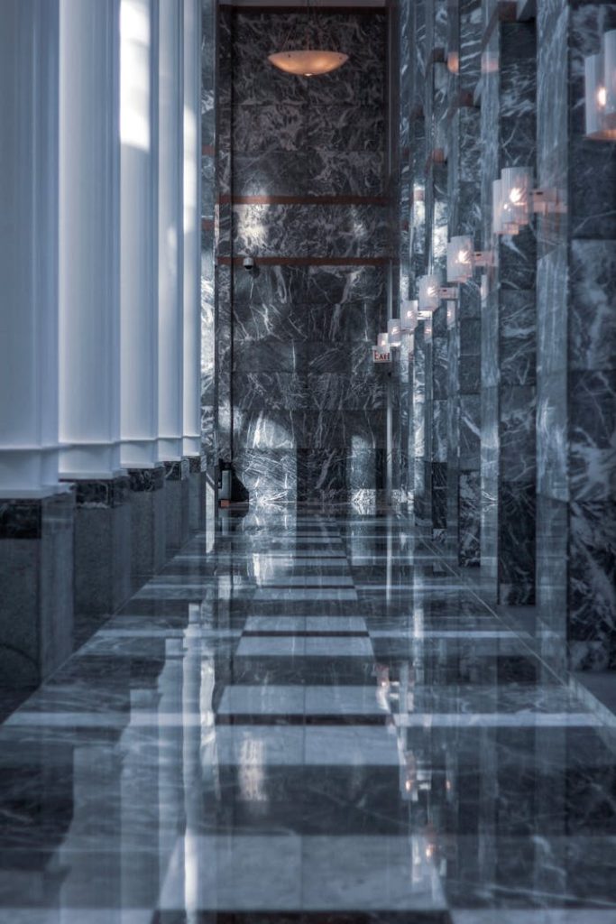 Sleek modern hallway featuring marble walls and floor with reflective surfaces and soft lighting.